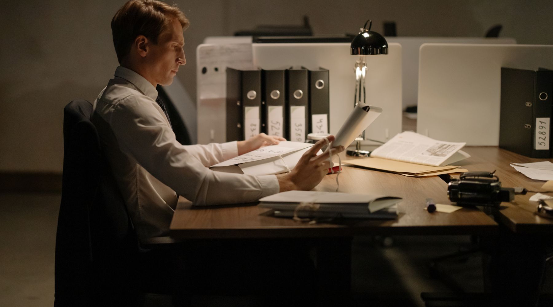 A person reading documents at a desk with folders and a lamp
