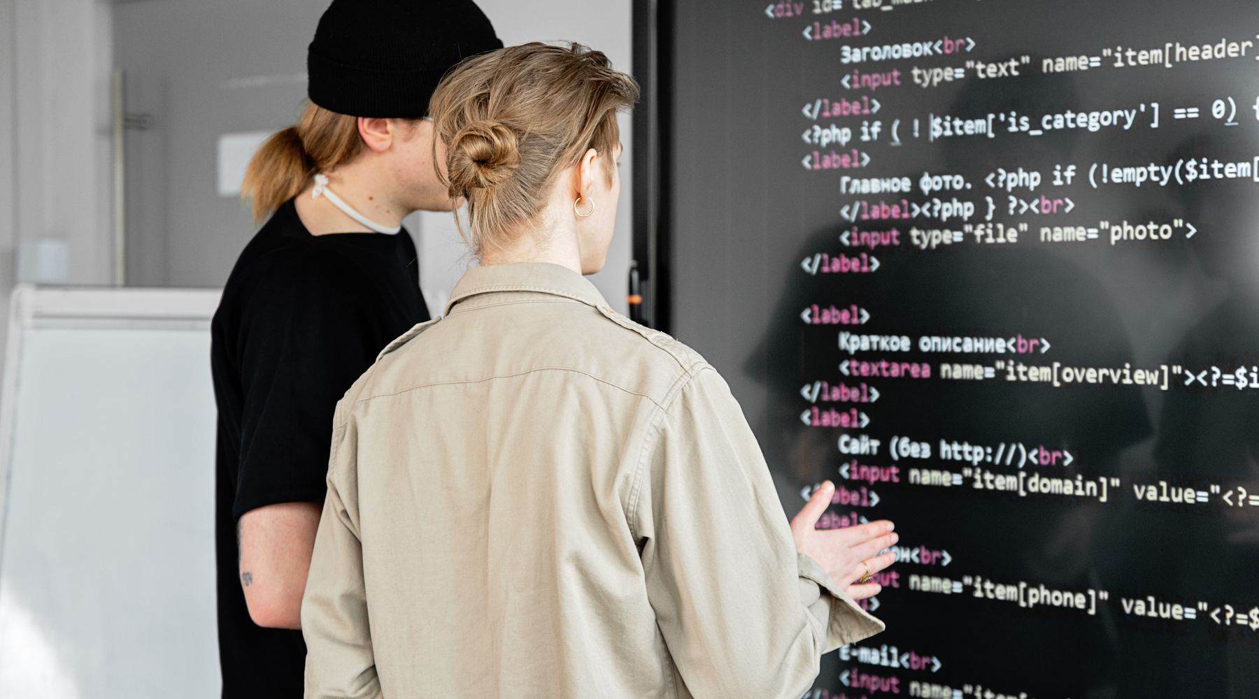 Two engineers examining code together on a large screen