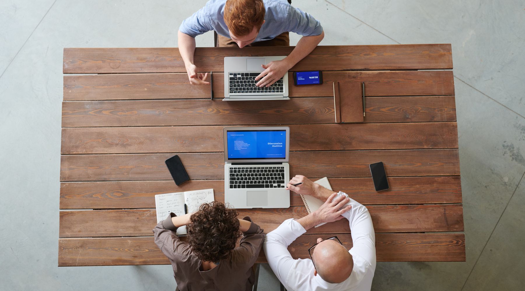 Three colleagues working with laptops at one wooden table